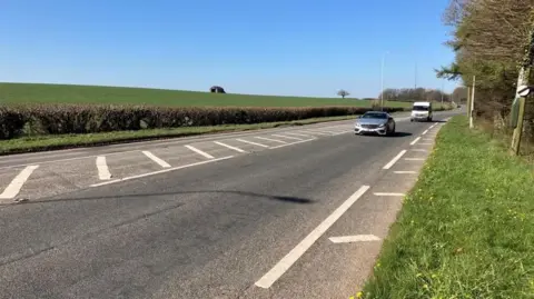 BBC The A48 near Bonvilston in the Vale of Glamorgan. A single lane with a car and a van travelling along it. A national speed limit sign is visible.