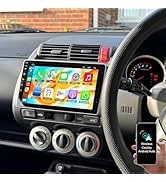 Car dashboard with touchscreen display showing Apple CarPlay interface with phone, music, home, and app icons; hand holding smartphone below steering wheel.