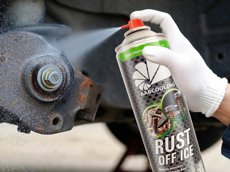 Gloved hand spraying aerosol product onto rusty metal bolt or fastener, with spray mist visible in the shot.