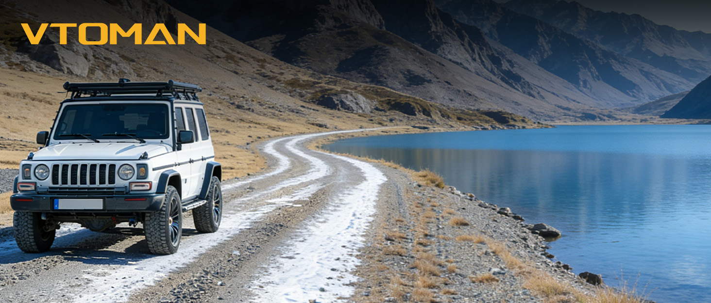 Text reads 'VTOMAN'. SUV vehicles driving on a winding road alongside a mountain lake, showcasing off-road capability in rugged terrain.