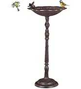Wooden bird feeder with green roof on stand. Features open tray for seeds, entrance hole, and hanging toy. Two birds approach the feeder.