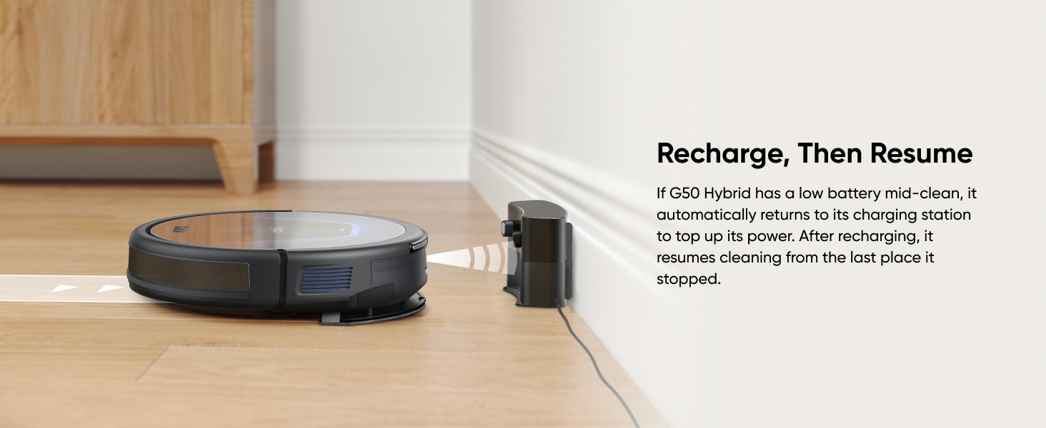 Black robotic vacuum cleaner on hardwood floor near white wall, with 'Recharge, Then Resume' text visible above.