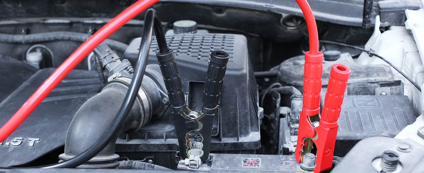 Car engine compartment with jumper cables attached, showing red and black clamps connected to the battery.