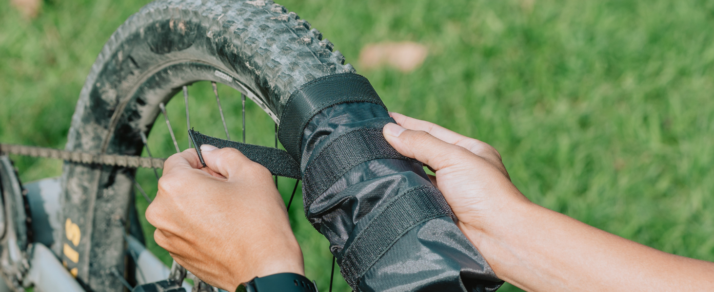 Close-up of hands cleaning or maintaining a muddy bicycle tire and frame with what appears to be cleaning equipment.