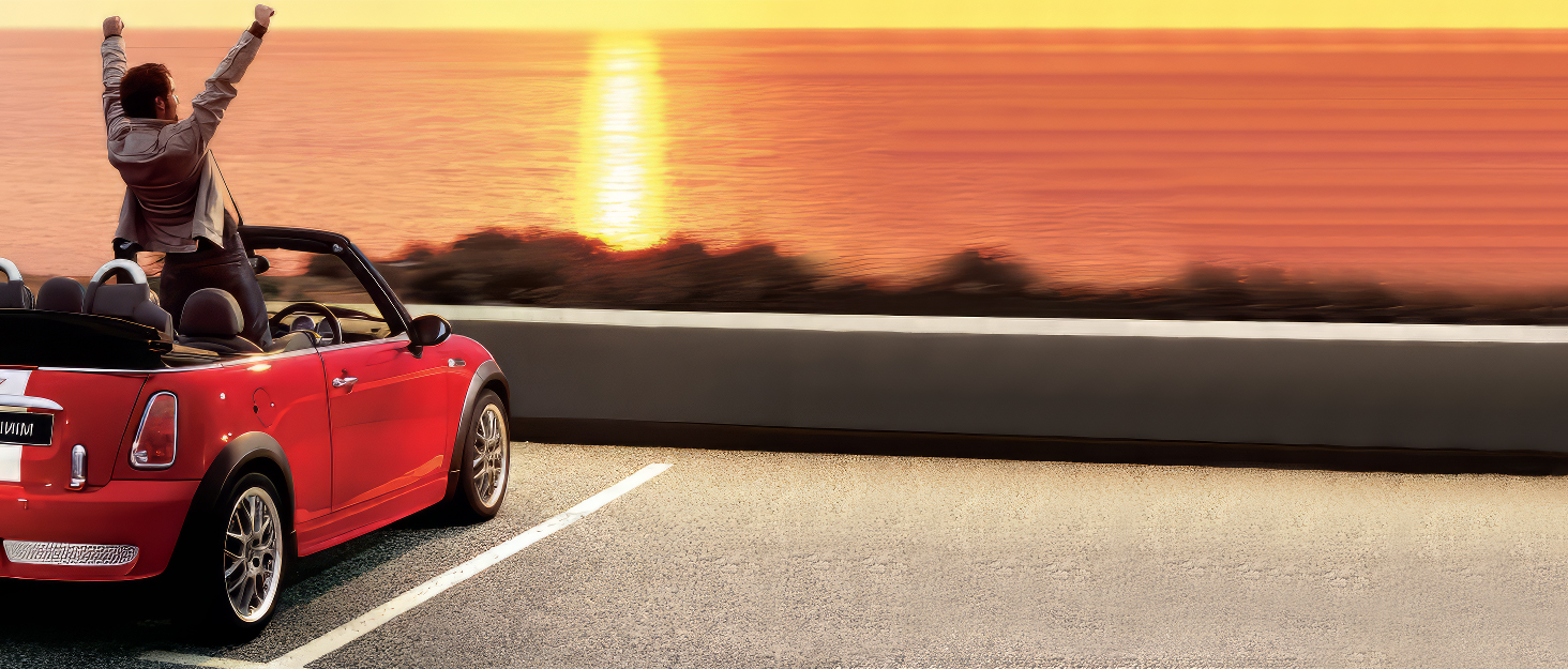 Red convertible car parked at sunset, with a person raising their arms in celebration, enjoying the scenic view of the ocean.
