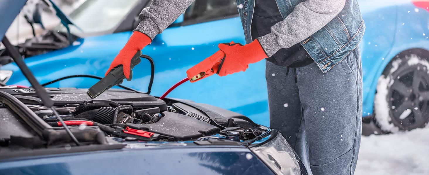 Person in red gloves using jumper cables on a car engine in snowy conditions, with blue car visible in background.