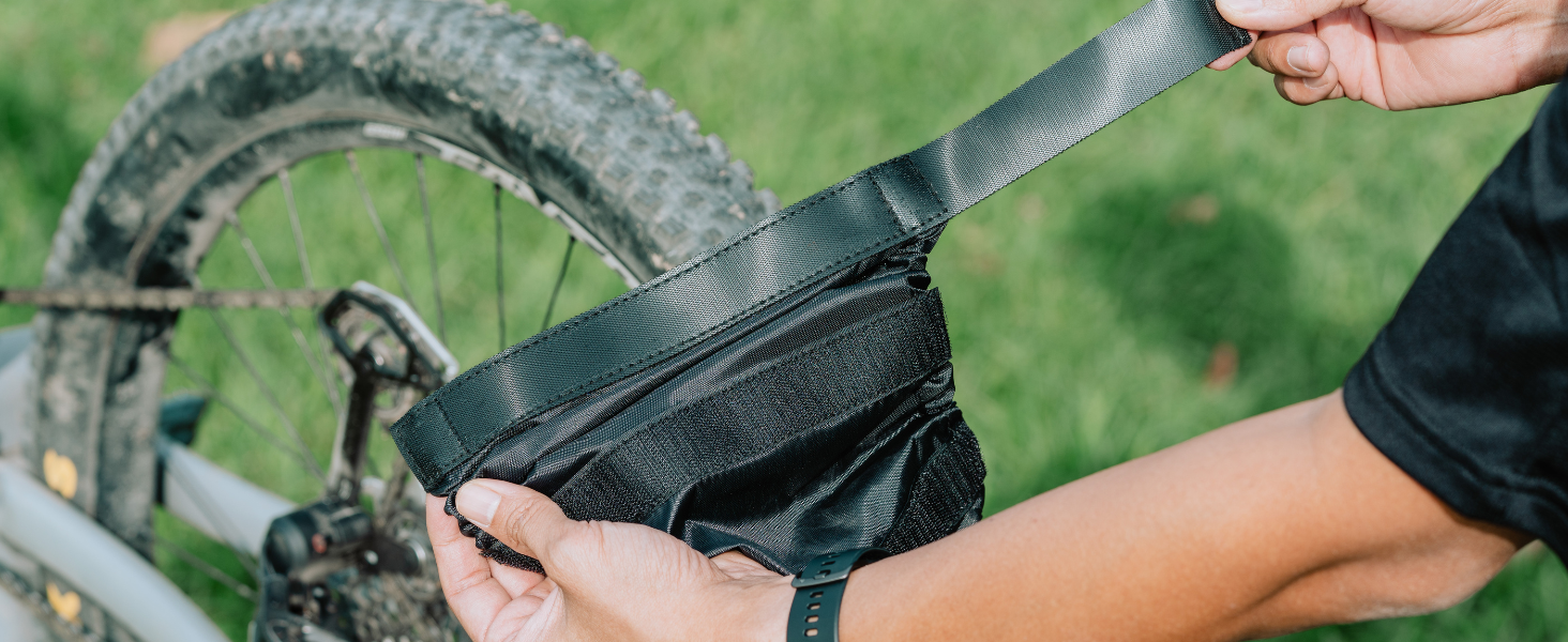 Close-up of hands adjusting or cleaning a bicycle component against a grassy background. Mountain bike tire and frame visible in the background.